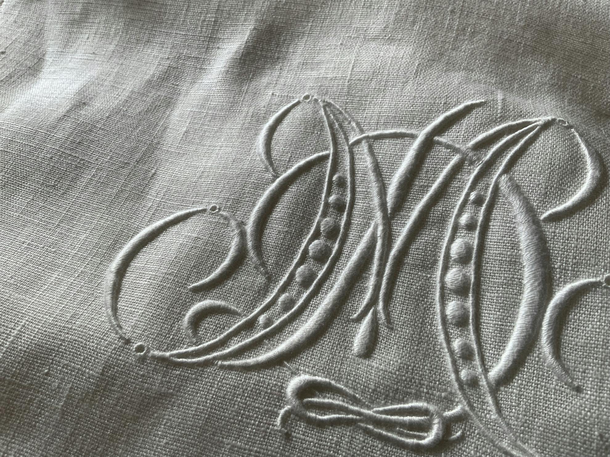 リネン布に刺された白糸刺繍のモノグラム刺繍